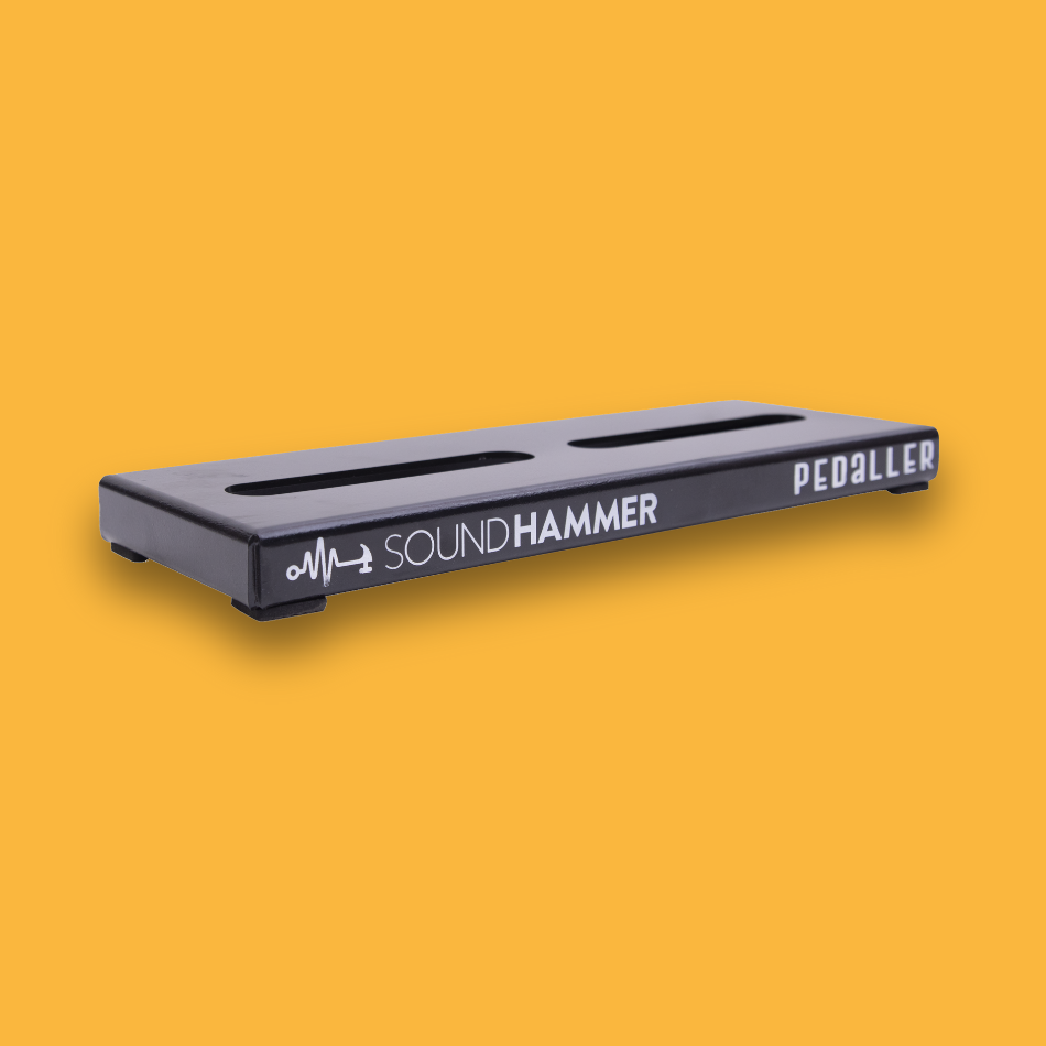 An angled view of a black guitar effects pedalboard made of single sheet of aluminium with two long holes for cable management and Soundhammer logo with rubber foot padding.