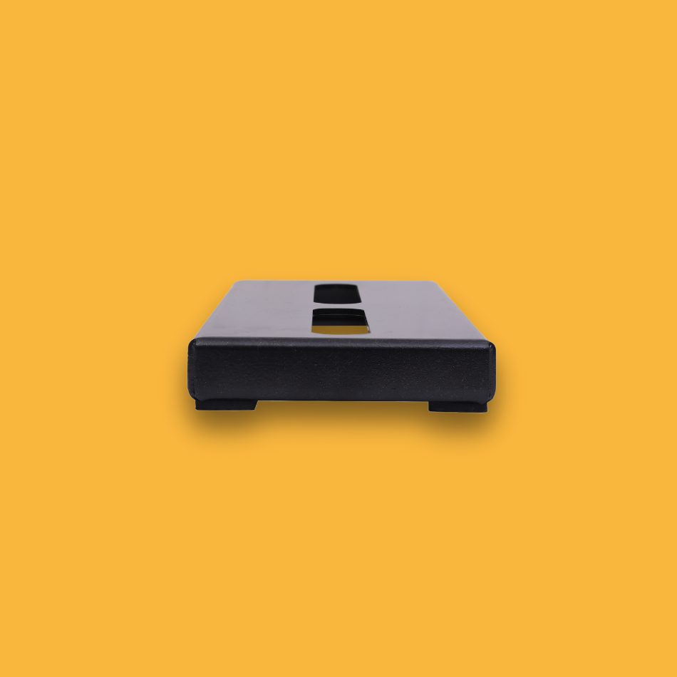 A side view of a black guitar effects pedalboard made of single sheet of aluminium with two long holes for cable management.