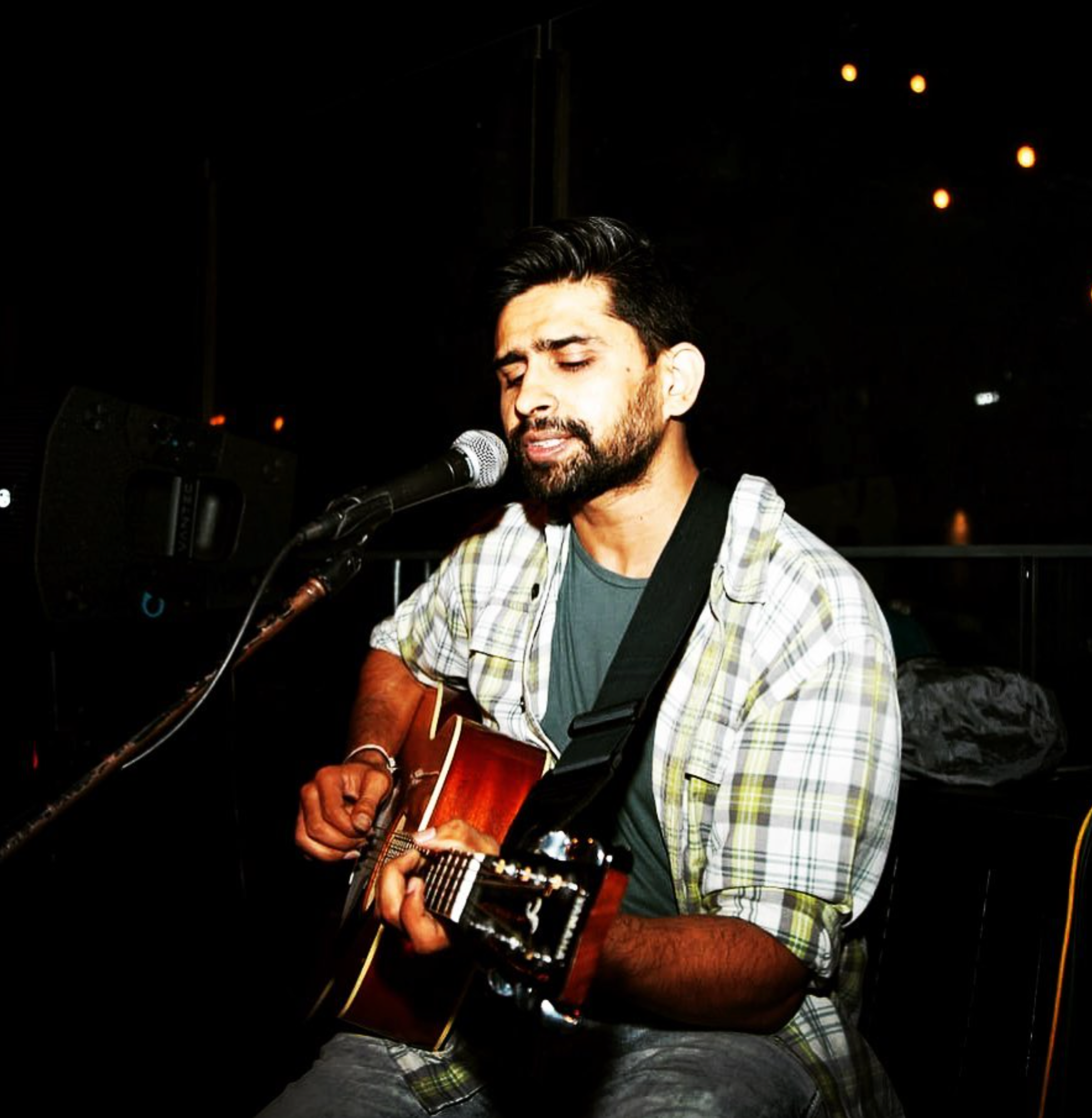 a singer songwriter with acoustic guitar singing in front of a mic