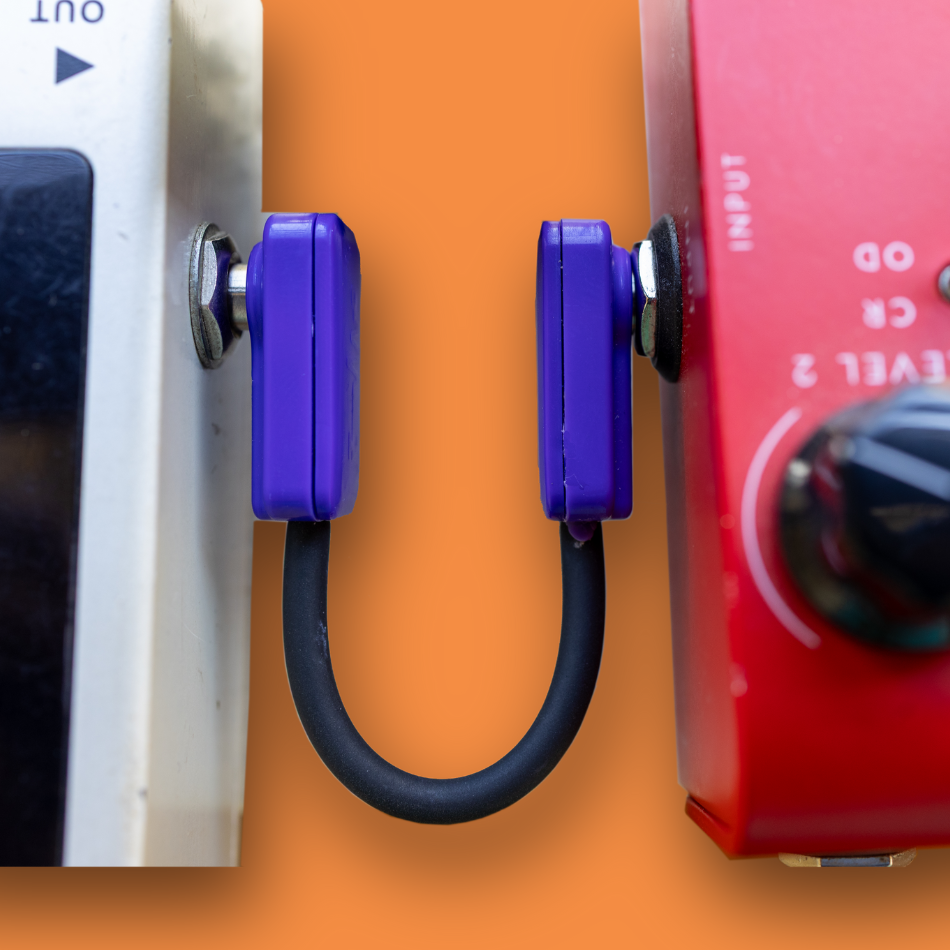 Two guitar effect pedals with a purple cable on an orange background