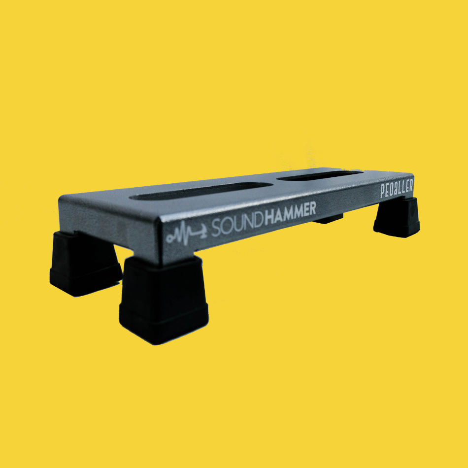 A side view of a lifted grey guitar effects pedalboard made of single sheet of aluminium with 4 legs and rubber bushings with Soundhammer logo.